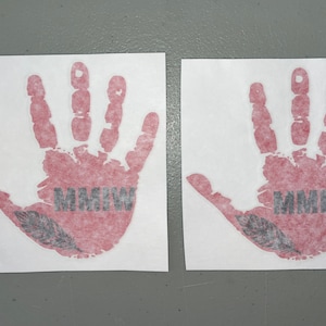 K&ouml;nnte beinhalten: Zwei rote Handabdruck-Aufkleber mit einer schwarzen Feder und dem Text "MMIW" auf wei&szlig;em Hintergrund.