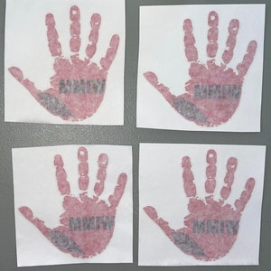 K&ouml;nnte beinhalten: Vier wei&szlig;e quadratische Aufkleber mit roten Handabdr&uuml;cken und dem Text "MMIW" in Schwarz. Die Handabdr&uuml;cke sind stilisiert, um wie ein Kinderhandabdruck auszusehen.