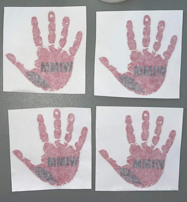 K&ouml;nnte beinhalten: Vier wei&szlig;e quadratische Aufkleber mit roten Handabdr&uuml;cken und dem Text "MMIW" in Schwarz. Die Handabdr&uuml;cke sind stilisiert, um wie ein Kinderhandabdruck auszusehen.