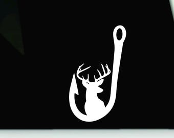 May include: A white vinyl decal featuring a silhouette of a deer head with antlers positioned inside the curve of a large fishing hook. The design is presented against a solid black background, creating a high-contrast graphic element.