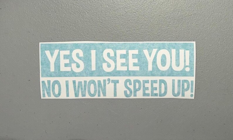May include: A rectangular bumper sticker with a light blue textured background and white bold sans-serif text that reads YES I SEE YOU! NO I WON'T SPEED UP! The sticker has a clean white border around the entire rectangular design.
