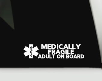May include: A white vinyl decal featuring the Star of Life medical symbol followed by the text "MEDICALLY FRAGILE ADULT ON BOARD" in bold, uppercase letters. The design is presented against a solid black background for high contrast visibility.