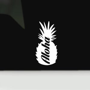 Op de afbeelding: Witte ananasafbeelding met het woord "Aloha" in een scriptlettertype. Het ontwerp staat tegen een zwarte achtergrond. De ananas is een symbool van gastvrijheid en tropische sferen.