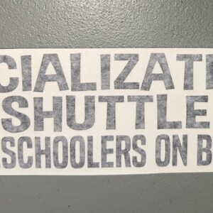 May include: A rectangular white bumper sticker featuring the dark gray text SOCIALIZATION SHUTTLE HOMESCHOOLERS ON BOARD in a bold sans-serif font. The text is arranged in three lines with a small eight-pointed star icon on each side of the middle line.