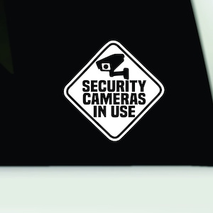 May include: White diamond-shaped sticker with a black silhouette of a security camera and the text "SECURITY CAMERAS IN USE".