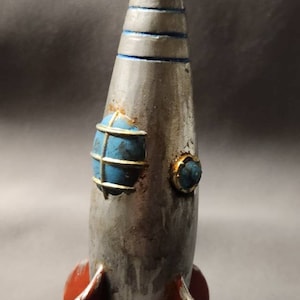 May include: A silver and red rocket ship toy with a blue and gold window. The rocket has three red fins and a pointed nose.