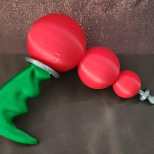 Puede incluir: Una herramienta manual con un mango ergonómico de color verde brillante con hendiduras para los dedos, conectada a una serie de tres componentes esféricos rojos graduados. El conjunto está asegurado con anillos plateados y una pequeña tuerca de mariposa.