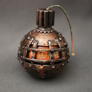 May include: A spherical object in a steampunk style, with a copper and bronze finish. It has a gear-shaped top, riveted metal bands, and a visible interior displaying the numbers "26" and "18". A twisted cord extends from the top.