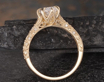 May include: A gold ring featuring a large, round, clear center stone held by a six-prong setting. The band is decorated with intricate, raised scrollwork patterns and small, embedded accent stones along the sides of the shank.