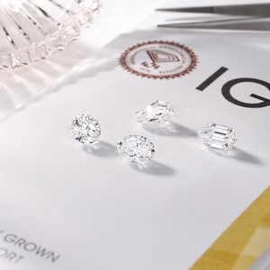 May include: Four sparkling, laboratory-grown diamonds of varying cuts are displayed on a white surface. The IGI logo and text are visible, along with a pair of tweezers and a decorative glass dish.