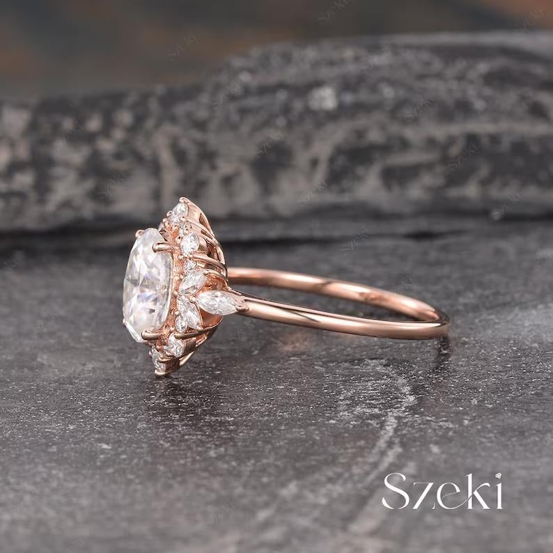 Pu&ograve; includere: Un anello di fidanzamento in oro rosa con una grande pietra centrale di forma ovale circondata da pietre pi&ugrave; piccole di forma rotonda e marquise. L'anello ha una fascia delicata.