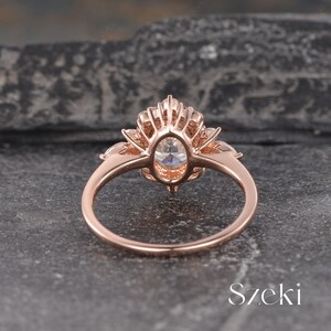 Pu&ograve; includere: Un anello di fidanzamento in oro rosa con una grande pietra centrale di forma ovale e pietre pi&ugrave; piccole su entrambi i lati. L'anello ha un design delicato e intricato con un motivo floreale.