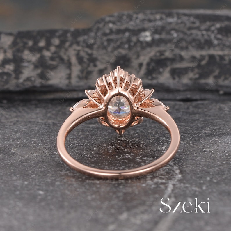 Pu&ograve; includere: Un anello di fidanzamento in oro rosa con una grande pietra centrale di forma ovale e pietre pi&ugrave; piccole su entrambi i lati. L'anello ha un design delicato e intricato con un motivo floreale.
