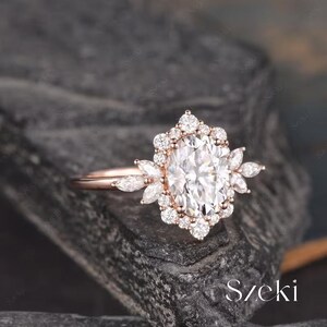 Pu&ograve; includere: Un anello di fidanzamento in oro rosa con una grande pietra centrale ovale circondata da diamanti pi&ugrave; piccoli. L'anello presenta un delicato motivo floreale con piccoli diamanti incastonati in un'aureola attorno alla pietra centrale.