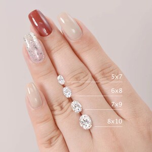 Pu&ograve; includere: Una mano di manichino con smalto per unghie neutro mostra cinque diamanti di forma ovale di diverse dimensioni. I diamanti sono etichettati con le loro dimensioni in millimetri: 5x7, 6x8, 7x9 e 8x10.