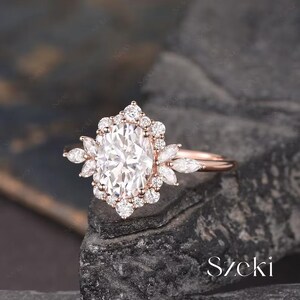 Pu&ograve; includere: Un anello di fidanzamento in oro rosa con una grande pietra centrale ovale circondata da diamanti pi&ugrave; piccoli. L'anello presenta un delicato motivo floreale con diamanti a forma di marquise sulla fascia.