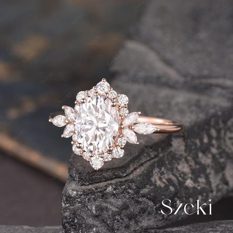 Pu&ograve; includere: Un anello di fidanzamento in oro rosa con una grande pietra centrale ovale circondata da diamanti pi&ugrave; piccoli. L'anello presenta un delicato motivo floreale con diamanti a forma di marquise sulla fascia.