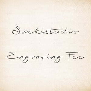 May include: A handwritten sign with the text "Szekistudio Engraving Fee".