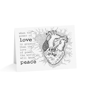 May include: A white greeting card with a black and white illustration of a human heart. The heart is filled with words in various languages. Text on the left side reads: "when the power of love is greater than the love of power, the world will know peace."
