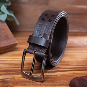 May include: A brown leather belt with a checkered pattern and a silver buckle. The belt is rolled up and the buckle is facing the camera.