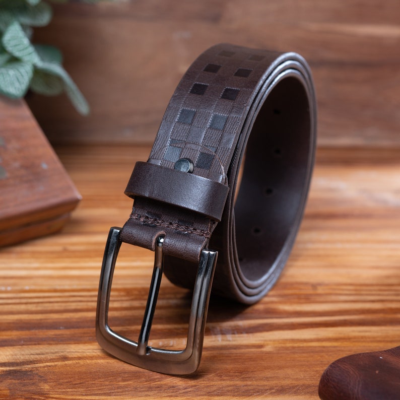 May include: A brown leather belt with a checkered pattern and a silver buckle. The belt is rolled up and the buckle is facing the camera.
