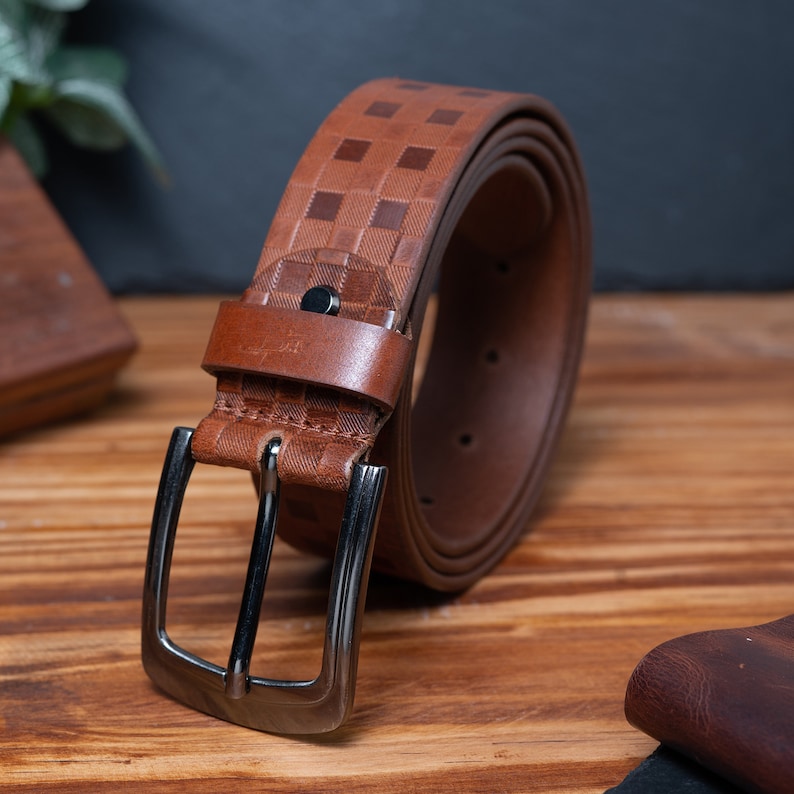 May include: A brown leather belt with a checkered pattern and a silver buckle.