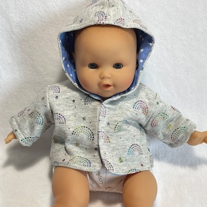 May include: A gray hooded sweater with a rainbow and star pattern for a baby doll. The sweater has a blue lining and is made of a soft, comfortable fabric.