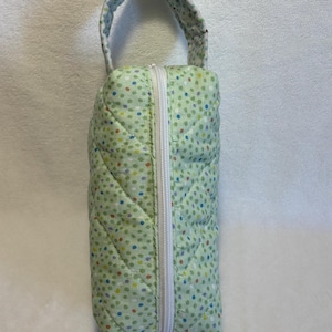 May include: A green quilted zippered pouch with a white zipper and a white handle. The pouch has a polka dot pattern with green, yellow, red, and blue dots.