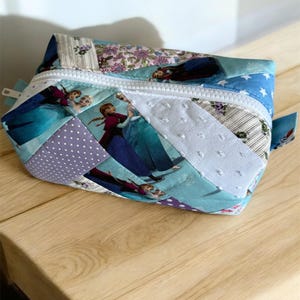 Può includere: Una pochette con cerniera in patchwork blu e viola con una stampa di personaggi di Frozen. La pochette è realizzata con diversi tessuti, tra cui pois, strisce e motivi floreali.