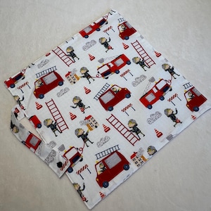 Peut inclure: Un sac en tissu carré avec un motif répétitif de pompiers en dessin animé, de camions de pompiers rouges, d'échelles, de cônes de signalisation orange et de bâtiments en feu sur un fond blanc. Le sac possède une petite poignée en tissu.
