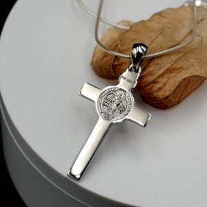 May include: Silver St. Christopher pendant necklace with a cross and a round medal featuring a saint. The medal has the words "Sanctus Christopher" and "Protector" on it.