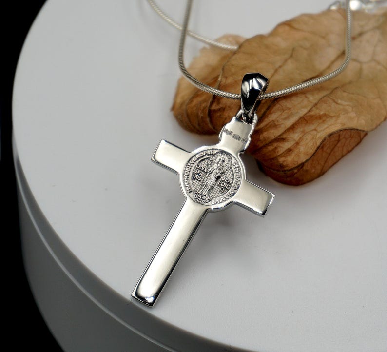 May include: Silver St. Christopher pendant necklace with a cross and a round medal featuring a saint. The medal has the words "Sanctus Christopher" and "Protector" on it.