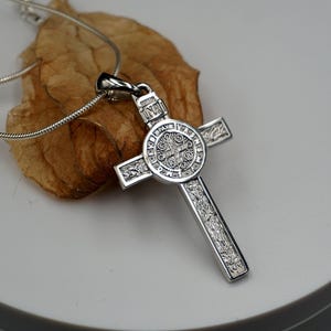 May include: Silver St. Christopher pendant necklace with a detailed cross design. The pendant features a circular medallion with intricate engravings.