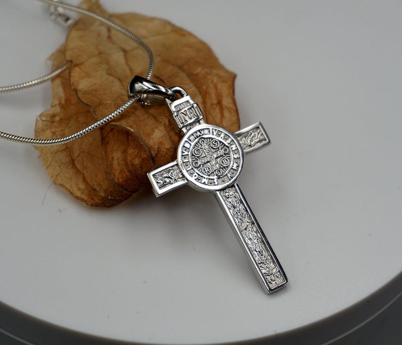 May include: Silver St. Christopher pendant necklace with a detailed cross design. The pendant features a circular medallion with intricate engravings.