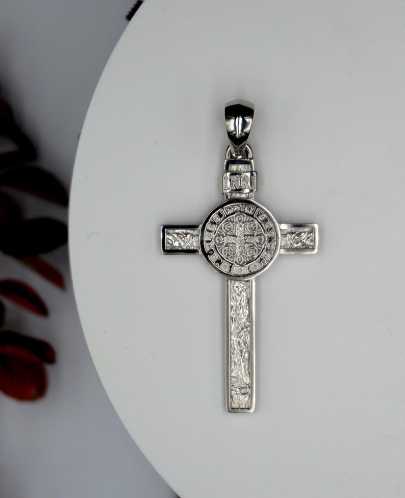 May include: Silver St. Christopher pendant with a detailed design. The pendant features a cross with a circular medallion in the center. The medallion has a detailed design of a saint and text around the edge.