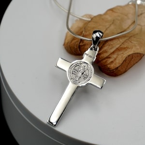 May include: Silver St. Christopher pendant necklace with a cross and a round medal featuring a saint. The medal has the words "Sanctus Christopher" and "Protector" on it.