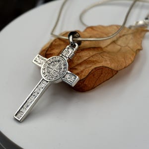 May include: Silver St. Christopher pendant necklace with a detailed cross design. The pendant features a circular medallion with intricate engravings.