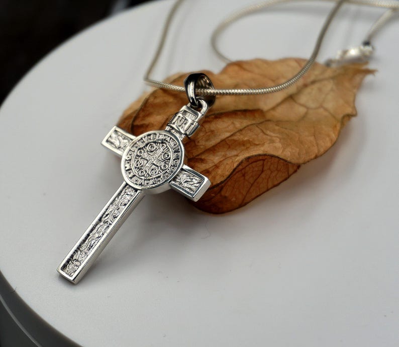 May include: Silver St. Christopher pendant necklace with a detailed cross design. The pendant features a circular medallion with intricate engravings.