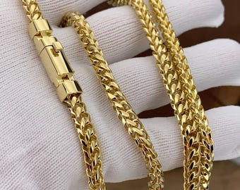 May include: A gold-toned franco chain necklace featuring a polished, interlocking V-shaped link pattern. The chain includes a rectangular box clasp mechanism with a secure locking hinge, showcasing a bright, reflective metallic finish throughout.