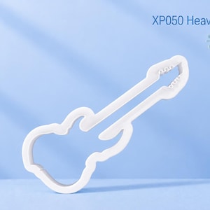 Könnte beinhalten: Ein weißer Ausstechform in Gitarrenform mit dem Text XP050 Heavy Metal Guitar. Das Objekt hat die deutliche Umrisslinie einer E-Gitarre mit einem langen Hals und einem konturierten Korpus, entworfen, um Teig in eine Musikinstrumentenform zu schneiden.