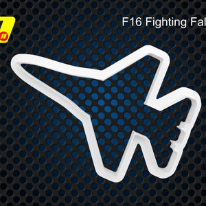 Op de afbeelding: Witte plastic koekjesvormer in de vorm van een F-16 Fighting Falcon straaljager. De koekjesvormer bevindt zich op een zwarte en blauwe achtergrond.