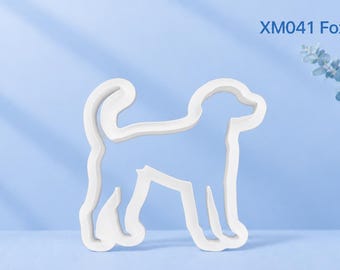 Puede incluir: Un cortador de galletas blanco con la forma de un perro de pie con la cola curvada. El texto XM041 Foxhound está impreso en la esquina superior derecha. El objeto tiene un contorno simple y limpio sobre un fondo de color azul claro.