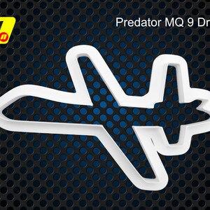May include: White plastic cookie cutter shaped like a Predator MQ 9 drone. The cutter is on a black and blue background.