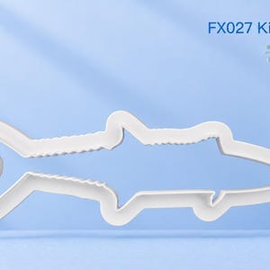 Pode incluir: Um cortador de biscoitos de plástico branco em forma de peixe, especificamente uma cavala real, com o texto FX027 King Mackerel impresso em azul no canto superior direito e um logótipo amarelo no canto superior esquerdo.