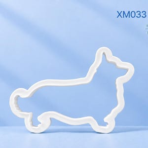 Könnte beinhalten: Ein weißer Ausstechform in der Form eines Welsh Corgi Hundes. Der Text XM033 Welsh Corgi ist in der oberen rechten Ecke aufgedruckt. Das Objekt zeigt eine saubere, durchgehende Kontur des Hundeprofils, einschließlich Ohren, Körper und Schwanz.