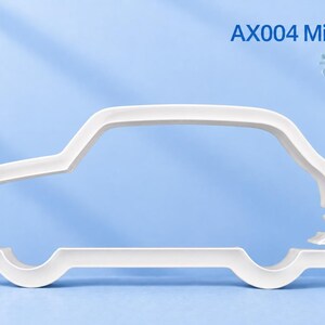 May include: A white plastic cookie cutter shaped like the silhouette of a car, featuring the text AX004 Mini Cooper S in the upper right corner. The design outlines the body of the vehicle with distinct wheel wells and a roofline profile.