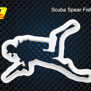 May include: White plastic cookie cutter shaped like a person spearfishing. The cookie cutter is on a black and blue background. Scuba Spear Fishing is written in white text at the top of the image.