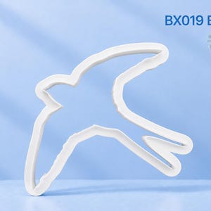 May include: A white plastic cookie cutter shaped like a barn swallow in flight. The text BX019 Barn Swallow is printed in the upper right corner. The object has a smooth, moulded outline of the bird with wings extended and a forked tail.