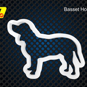 Könnte beinhalten: Weißer Plastik-Ausstecher in Form eines Basset-Hundes. Der Ausstecher befindet sich auf einem schwarzen Hintergrund mit einem blauen Gittermuster.