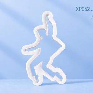Puede incluir: Un cortador de galletas blanco con forma de persona bailando con un brazo levantado y una pierna doblada, que incluye el texto XP052 Jailhouse Rock. El objeto tiene un acabado mate liso y un contorno definido que marca la silueta.